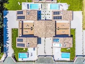 Vista aérea de um resort com várias piscinas, espreguiçadeiras e painéis solares.