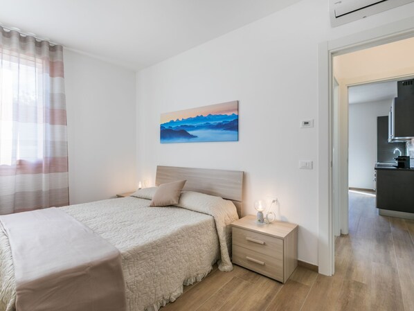 Un dormitorio con cama, mesitas de noche, una pintura y vistas a la cocina.