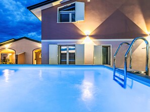 Una casa moderna con piscina, un porche cubierto e iluminación exterior.