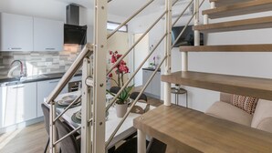 A modern kitchen with white cabinets, a stainless steel sink, and a wooden staircase leading to a dining area with a table and chairs. - Borgo il Vallin delle Conche by Interhome (Cecina)