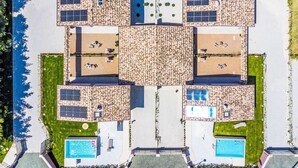 Vista aérea de un complejo turístico con varias piscinas, tumbonas y paneles solares.