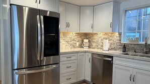 Uma cozinha moderna com eletrodomésticos de aço inoxidável, armários cinza claro e painel de azulejos.