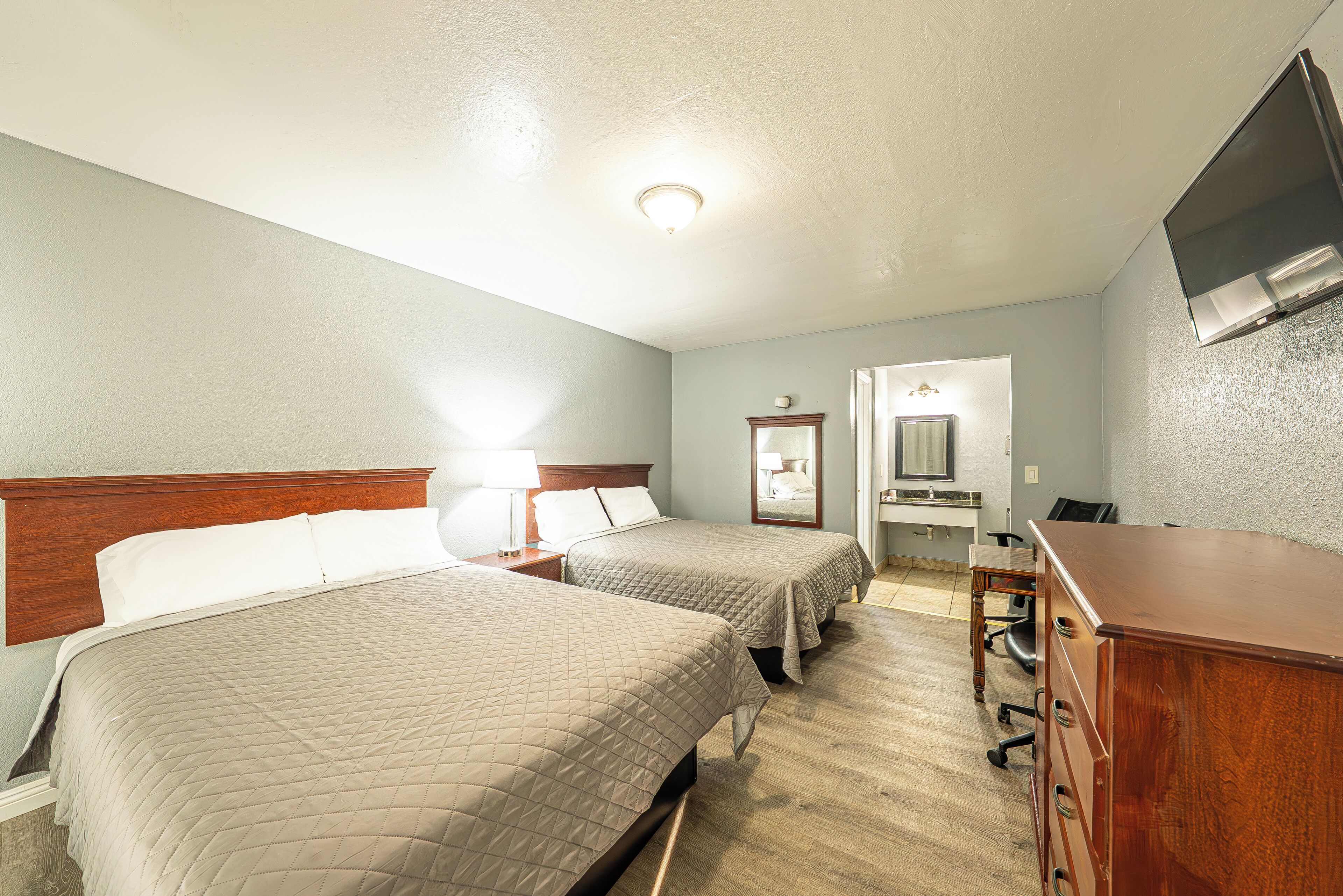 Une chambre d’hôtel avec deux lits « queen size », une commode en bois, un bureau et un téléviseur fixé au mur.