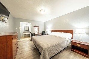 A hotel room with a bed, a wooden dresser, a desk with a chair, and a nightstand with a lamp. - Villa Motel (Santa Maria)