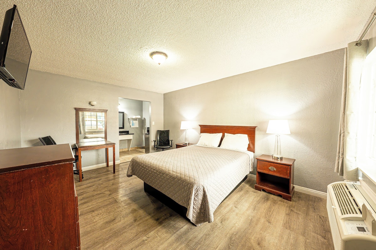 Habitación de hotel con cama, mesitas de noche, escritorio, silla y televisión.