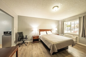 Une chambre d’hôtel avec un lit, deux lampes de chevet, un bureau avec un ordinateur, une chaise et une fenêtre avec des rideaux.