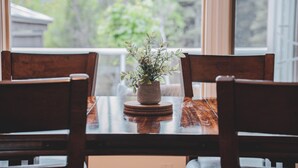 A wooden dining table with a potted plant in the center, surrounded by wooden chairs.