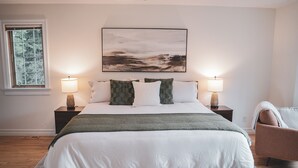 A bedroom with a large bed, two bedside lamps, a window with a view, and a painting on the wall.