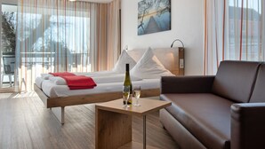 A modern hotel room with a bed, a wooden nightstand, a glass table with a bottle and glass, a brown leather sofa, and large windows with curtains. - Apartment 'Typ A2 2 Obergeschoss Nummer 13' with Shared Terrace, Shared Garden and Wi-Fi (Immenstaad am Bodensee)