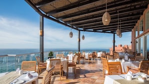 Un área de comedor al aire libre con mesas y sillas, con vista al mar.