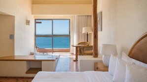 Habitación de hotel con un ventanal grande que ofrece vistas al mar, una cama, un escritorio y una silla.