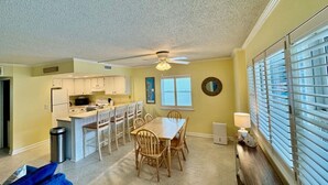 A compact kitchen with white cabinets, a dining area with a wooden table and chairs, and a ceiling fan.