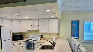 A kitchen with white cabinets, a stove, a microwave, a sink, and a long countertop.