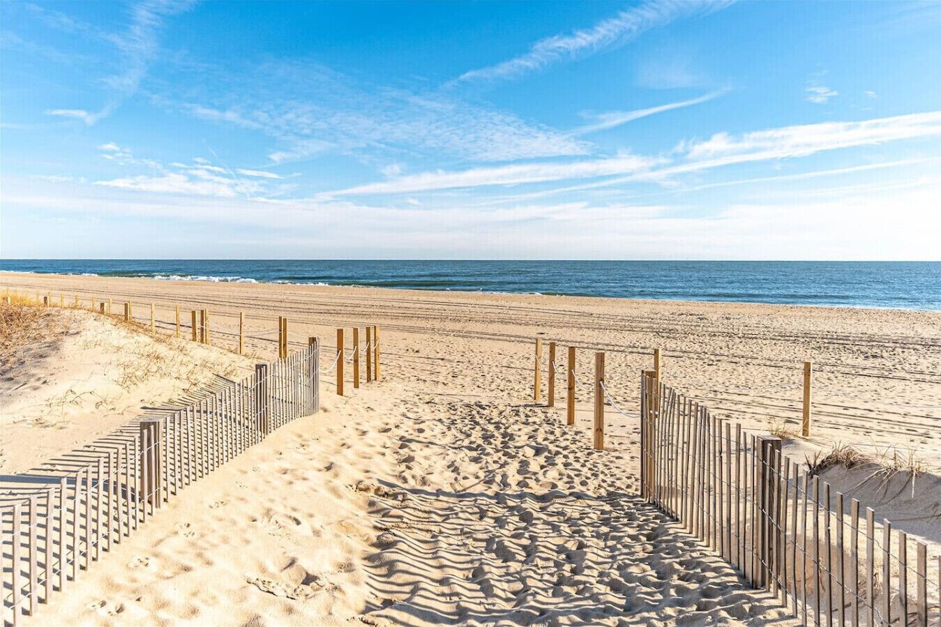 Une plage de sable bordée de clôtures en bois, sous un ciel bleu et dégagé.
