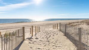 Ein Sandweg am Strand mit Holzzaun, der zum Meer führt.