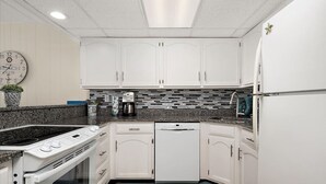 Eine Küche mit weißen Schränken, einer Granit-Arbeitsplatte, einer Kaffeemaschine, einem Geschirrspüler und einer Uhr an der Wand.