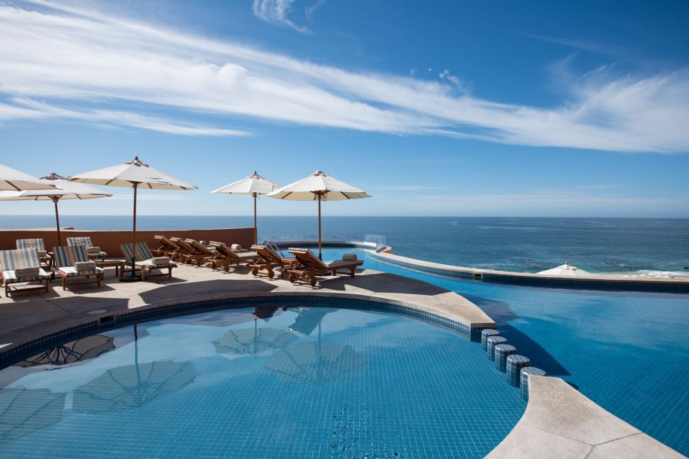 Ein Poolbereich mit Liegestühlen und Sonnenschirmen mit Blick auf den klaren, blauen Ozean.