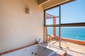 A bathroom with a large window, a bathtub, and a view of the sea.