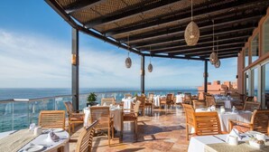 An outdoor dining area with tables and chairs, overlooking the sea.