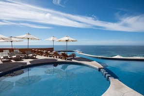Ein Poolbereich mit Liegestühlen und Sonnenschirmen mit Blick auf den klaren, blauen Ozean.