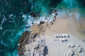 An aerial view of a beach with a row of white umbrellas and a rocky shoreline.