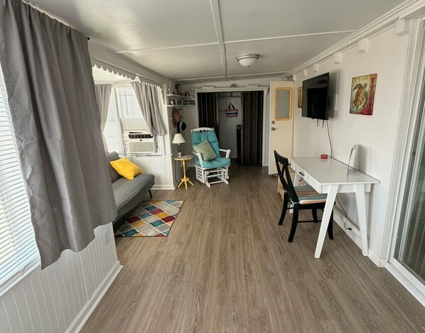 A compact living space with a sofa, a small table, a chair, and a television mounted on the wall.