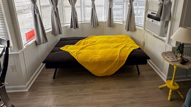 Ein Schlafzimmer mit einem Bett, einem Fenster mit Vorhängen, einem Heizkörper und einer Lampe auf einem kleinen Tisch.
