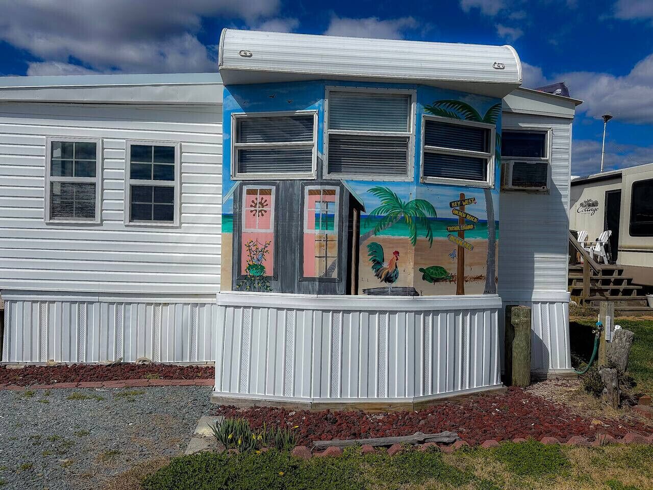 Una casa móvil con un exterior colorido, que incluye un mural con una escena de playa y un gallo.