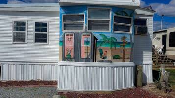Una casa móvil con un exterior colorido, que incluye un mural con una escena de playa y un gallo.