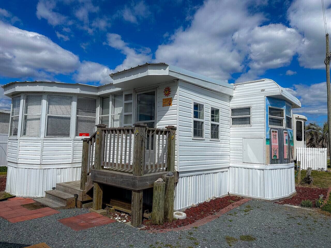 Una casa móvil blanca con un porche de madera y una pequeña terraza, que cuenta con una puerta y ventanas.