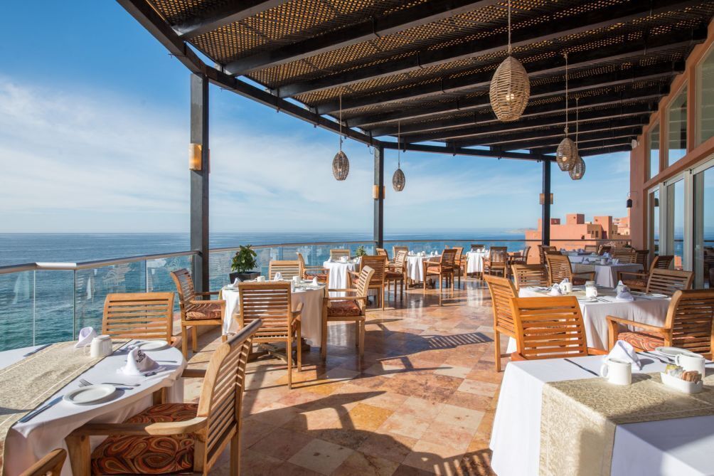 Un espace extérieur aménagé pour les repas, avec des tables et des chaises, offrant une vue sur la mer.