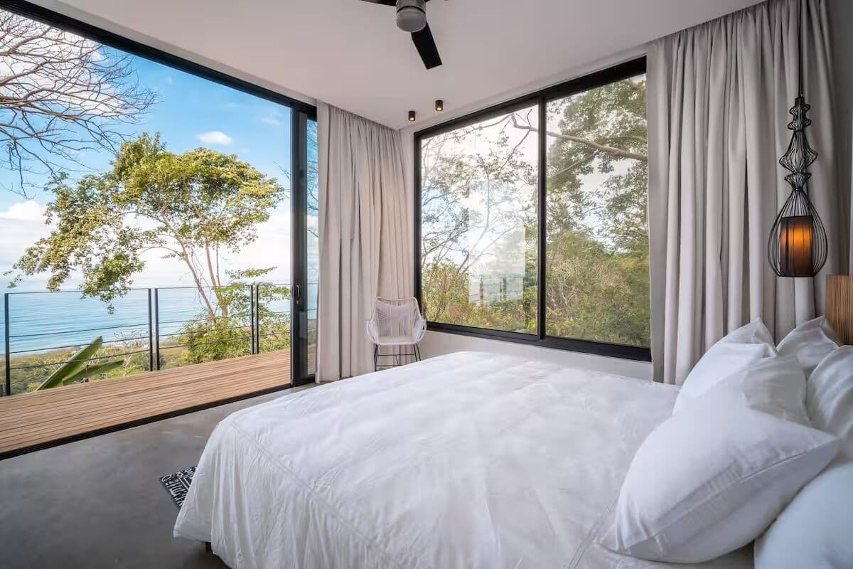 A bedroom with a large window, a bed, a chair, and a ceiling fan.