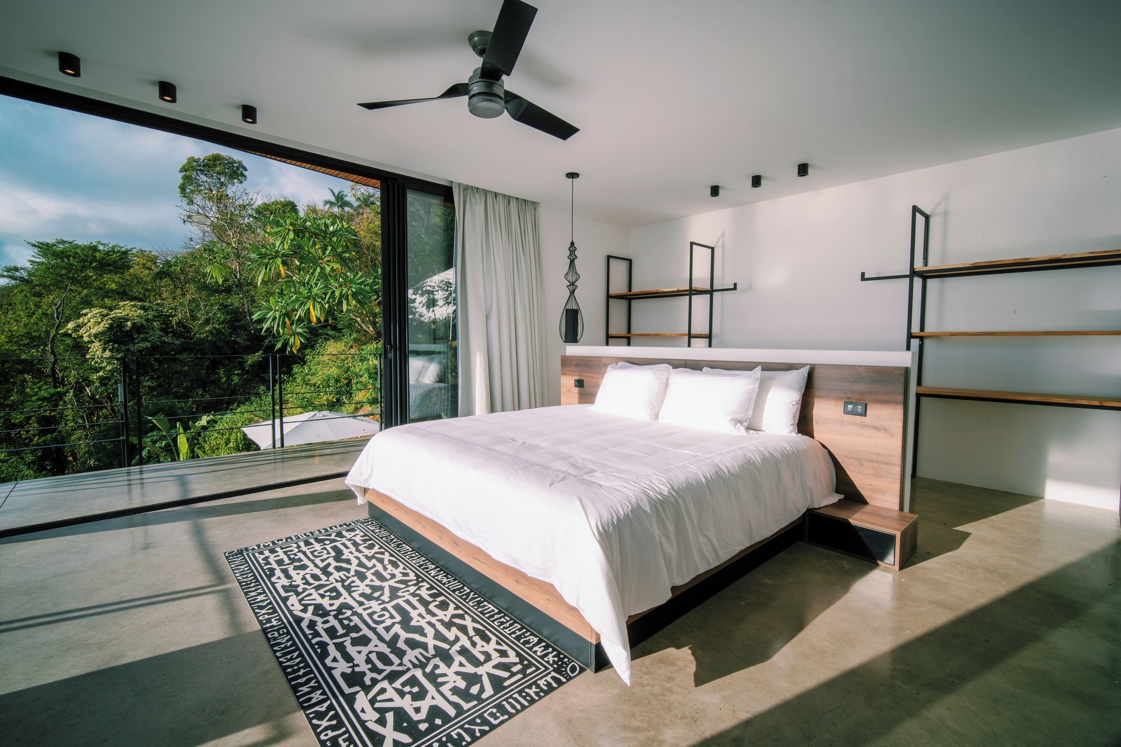 Camera moderna con un letto grande, una ventola a soffitto e vista su un lussureggiante spazio verde.