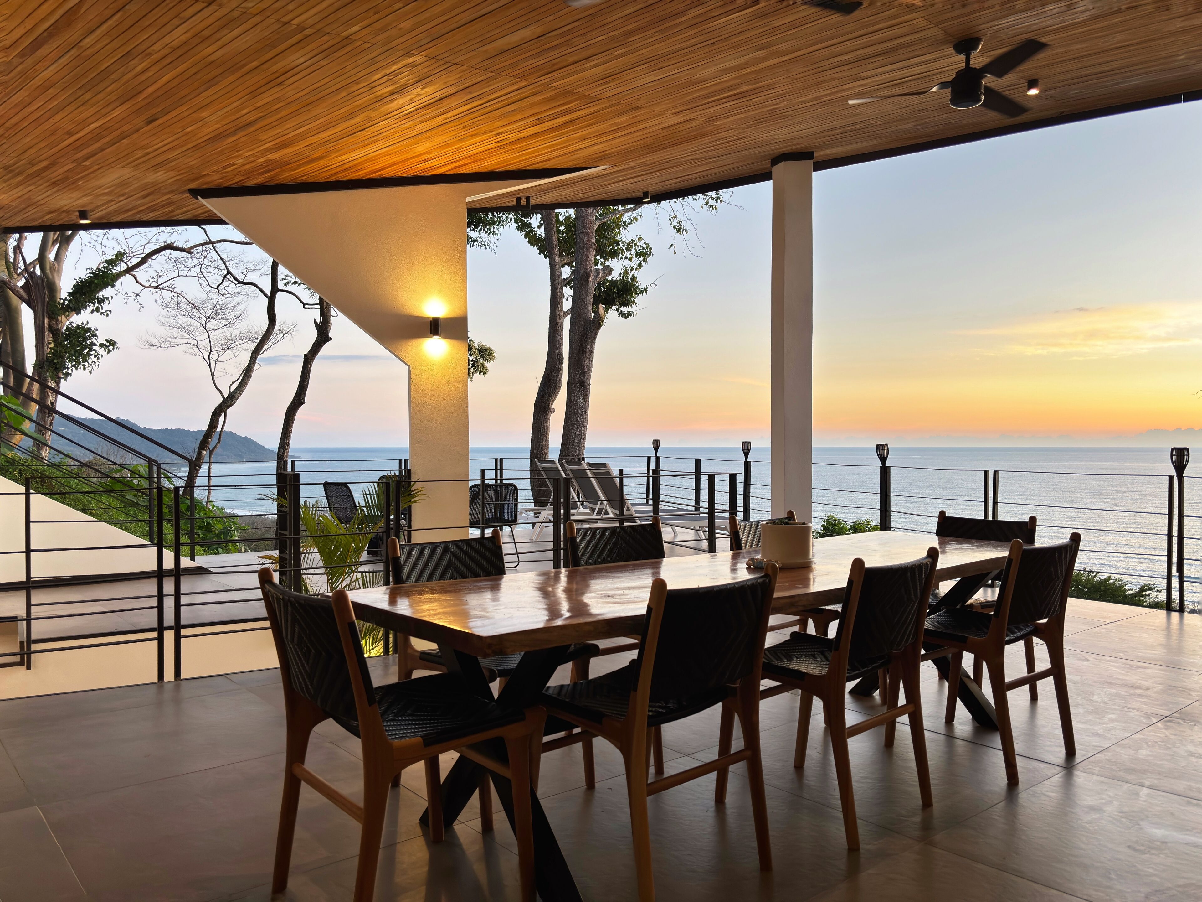 Een terras met een houten tafel en stoelen, met uitzicht op een schilderachtig zeegezicht.