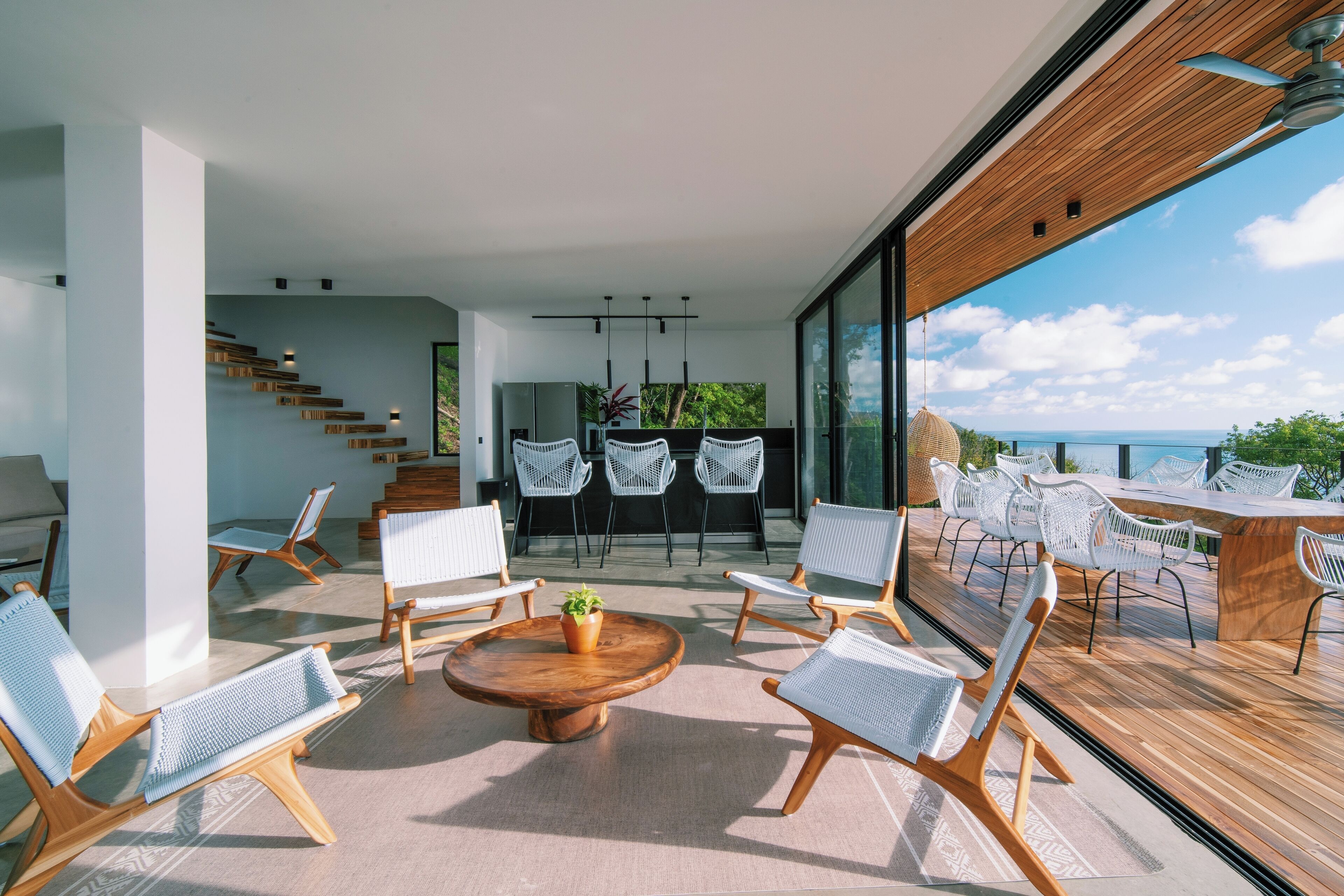 Ein modernes Interieur mit einer Essgegend aus Holz, weißen Stühlen und Blick auf das Meer.