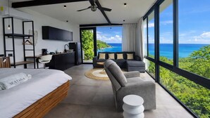 Ein modernes Schlafzimmer mit Bett, Schreibtisch, einer Couch und Meerblick.