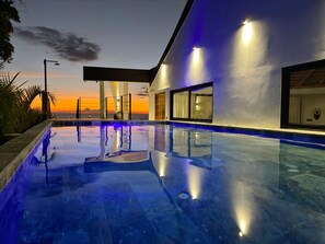 Un espace piscine moderne offrant une vue dégagée sur le coucher de soleil et l’océan en arrière-plan.