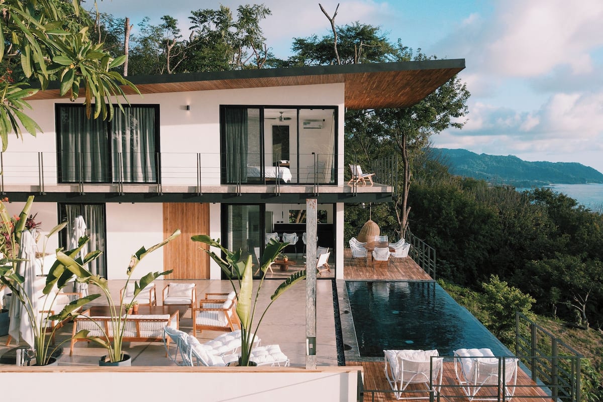 A modern two-story house with a large balcony, a pool, and a view of the sea.