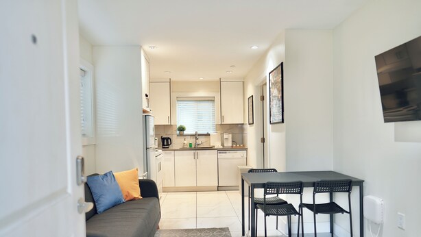 A compact living space with a kitchenette, a dining area with a table and chairs, and a sofa with cushions.