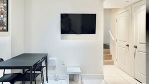 A modern room with a flat-screen TV mounted on the wall, a dining table with chairs, and a small white side table.