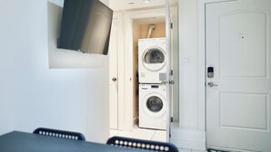 A laundry room with stacked washers and dryers, a television mounted on the wall, and a door with a lock.