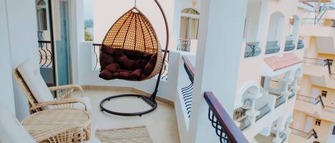 A balcony with wicker furniture, a hanging chair, and a view of neighboring buildings.