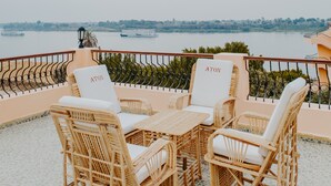 Un balcon agrémenté de meubles en osier, une vue sur un lac et un bateau aperçu au loin.