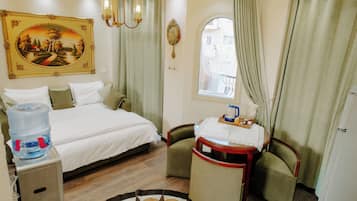 A hotel room with a bed, a desk with a chair, a water dispenser, a painting, a window, and a chandelier.