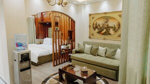 Une chambre d’hôtel comprenant un lit, un canapé, une table basse, un distributeur d’eau, une armoire en bois et un tableau au mur.
