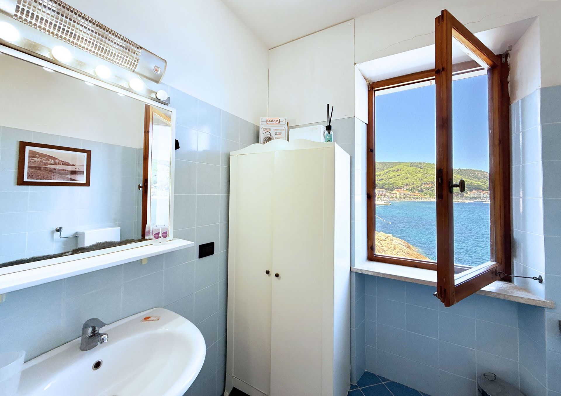 Une salle de bain avec une baignoire, un lavabo, un miroir et une fenêtre donnant sur la mer.