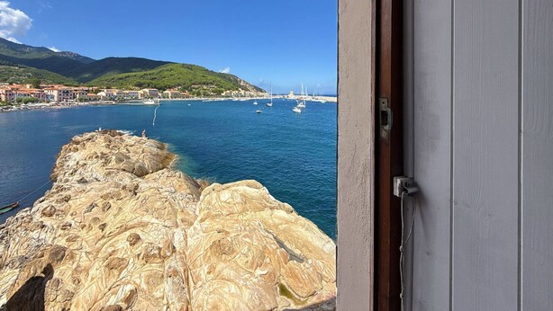 A coastal view from a room with a view of the sea, rocky shoreline, and distant buildings.