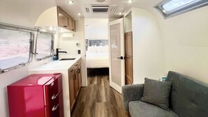 Interior compacto de uma motorhome, com cozinha compacta, área de refeições, sofá cinza e uma pequena janela.