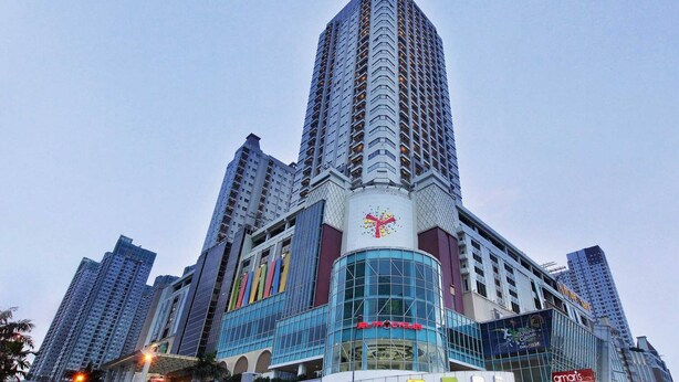 A high-rise building with a prominent glass facade, multiple balconies, and a central logo. - Apartemen Thamrin City 1 BR City View (Jakarta)