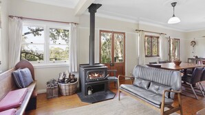 Uma sala de estar aconchegante com lareira, um sofá, uma mesa de jantar e janelas amplas com vista para o exterior.